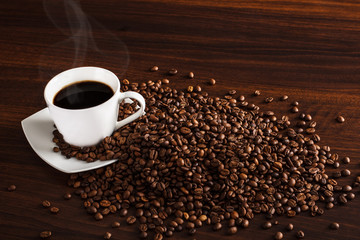 Coffee beans with cup of coffee and steam.