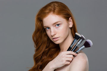 Attractive young redhead woman holding set of makeup brushes