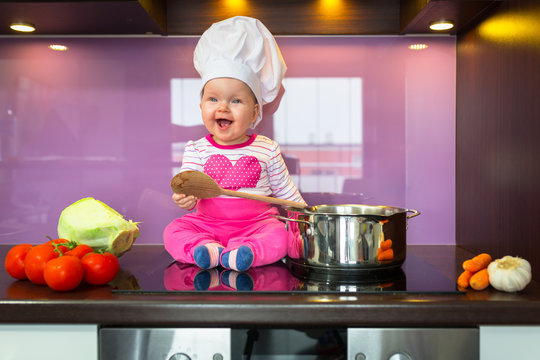 Little baby girl cook in chef hat at the kitchen