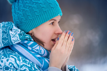 portrait girl in a blue cap and jacket warms her hands in the cold winter