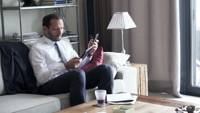 Businessman comparing data on tablet computer and smartphone at home

