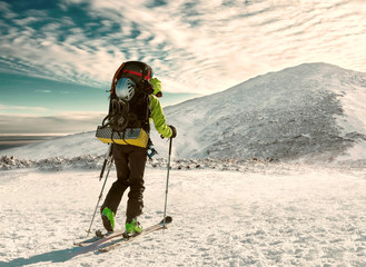 Men with backpack at ski goes to the top of mountain in sun day