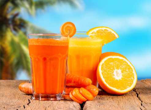 Fresh juices, orange and carrot on wooden table with tropical beach background