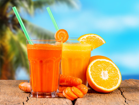 Fresh juices, orange and carrot on wooden table with tropical beach background