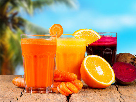 Fresh juices, orange, beetroot and carrot on wooden table with tropical beach background