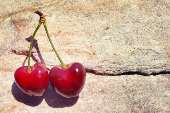 Two berries of red ripe fresh sweet cherry on a stone. Romantic couple. Valentine's Day card. Two juicy cherries in the form of heart