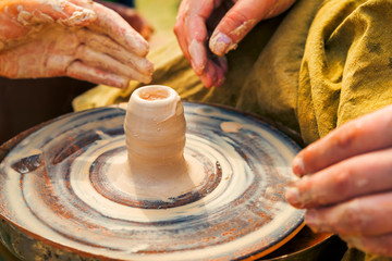 potters hands guiding a men hands to help him to work with the clay