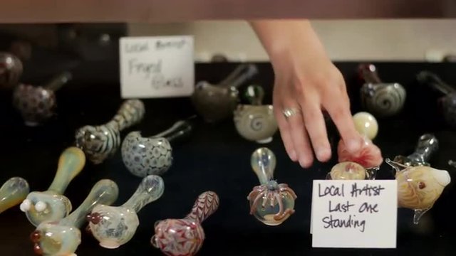 Close up of glass pipes in a case in a retail marijuana shop, and an associate taking it out to show customers