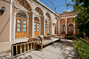 Fototapeta na wymiar Green courtyard of beautiful iranian mansion with Ottoman beds for relaxation