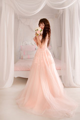 Fototapeta premium Beautiful young bride in her wedding dress peach, looking down.The gentle light bedroom.Wedding in pink.