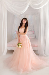 Beautiful young bride in her wedding dress peach, looking down.The gentle light bedroom.Wedding in pink.