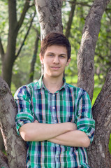 a young man in a plaid green shirt posing near a tree in the summer park