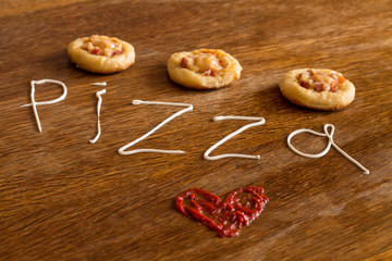 Three mini pizzas with sausage and cheese on wood table. Painted heart of ketchup and written text 