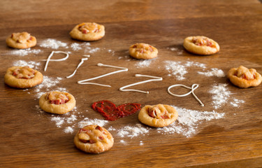 Mini pizzas with sausage and cheese on wood table.  Painted heart of ketchup, written text "pizza" of mayonnaise and flour.