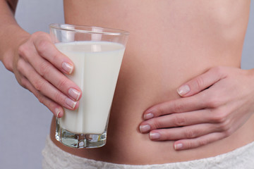 Woman with stomach pain holding a glass of milk. Dairy Intolerant person. Lactose intolerance, health care concept. Selective focus on glass of milk - obrazy, fototapety, plakaty