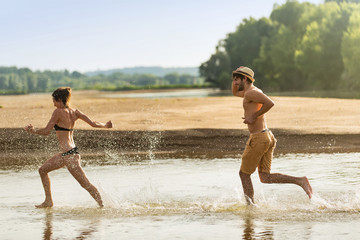 Fototapeta na wymiar Water is splashing around a couple running at the beach during the holidays