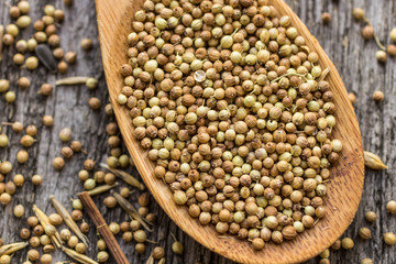 Dried coriander seeds in wooden spoon on old wooden table