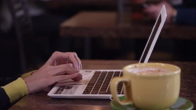 Up close panning view of person using touch pad on laptop in coffee shop.