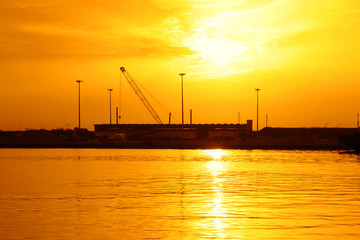 Tramonto giallo sul mare con una gru di cantiere sullo sfondo