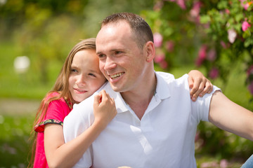 Beautiful young father and small pretty daughter embrace outdoors