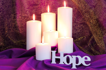 Hope by white candles with purple and gold fabric background