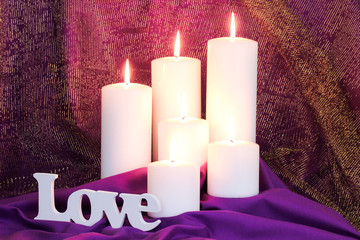 Love by white candles with purple and gold fabric background