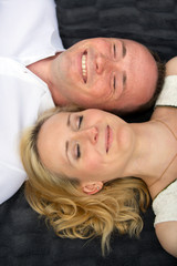 Happy and smiling couple with closed eyes lies on a gray plaid