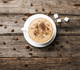 Close-up of coffee cup with roasted coffee beans on wooden backg