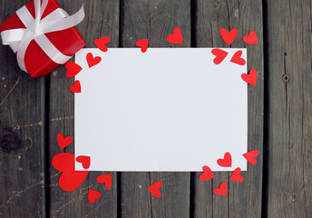 Red present and white paper on wood table with hearts mockup