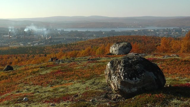 Autumn bright red hills with low polar vegetation and large rocks, the city and the bay beyond.