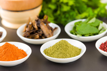 Beautiful colorful display of different spices green orange brown in white bowls, shot from above side angle, grey background
