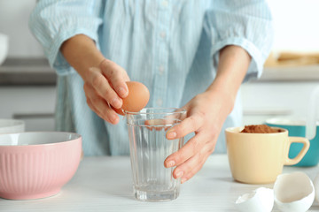 Woman is breaking an egg into a glass