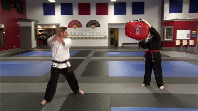 Man kicking a bag held in the air at a karate studio.