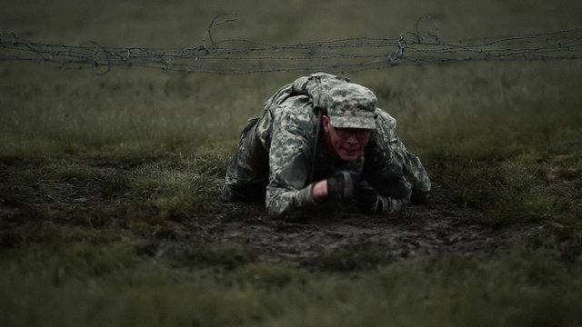 Soldier crawling under low barbed wire on elbows and knees.