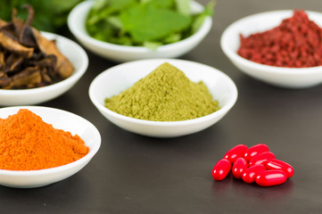 Beautiful colorful display of different spices green orange brown in white bowls, shot from above side angle, grey background