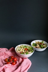 Salad made with lettuce, cherry tomatoes, radish, chicken and pasta. Dark background, selective focus, copy space.