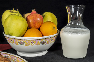 Ceramic bowl full of fruits beside a glass jar with milk