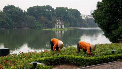 Two workers pluck weeds in front of Turtel Tower, Vietnam