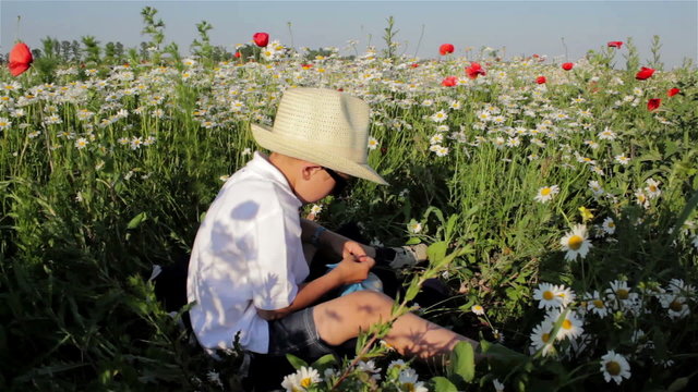 a boy with a hat/boy sits in a hat in a field between the flowers and eating a sandwich