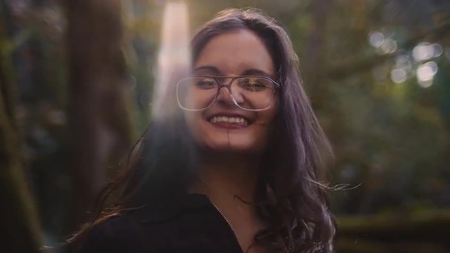 Beautiful girl in a forest throws leaves up in the air and laughs, slow motion, bokeh and lens flare