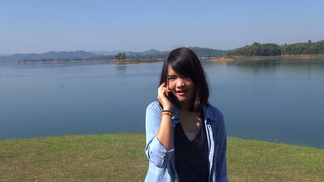Cute young woman in the mountains in front of lake talking on the phone smile.