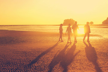 The family walking at the beach during sunset time, orange sun light, like instagram filter effect
