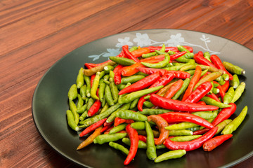 A lot of chili peppers on black dish. Wooden background.