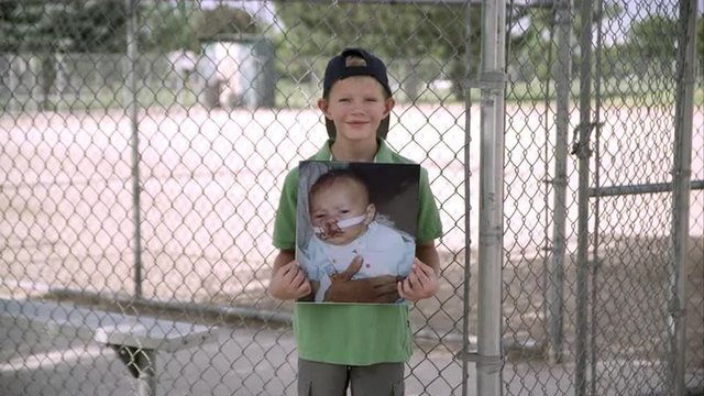Slow motion push of boy holding up picture of himself as baby and smiling.