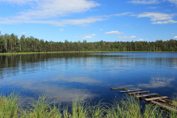 round forest lake with wooden brige in sunny weather with blue sky and small clouds