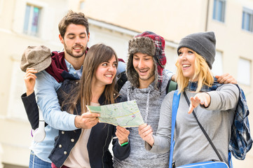 Group of young hipster tourists friends cheering with city map in the old town - Travel lifestyle concept with happy people having fun together - Winter fashion clothing wearing

