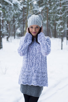 The woman poses outdoors in the winter wood, in a knitted pullover and a hat with ears