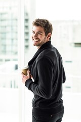 Handsome man holding disposable cup looking back to camera