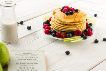 Stack of Sweet Pancakes with Fresh Blueberry, Raspberry, Apple and Maple Syrup on White Light Background, Horizontal