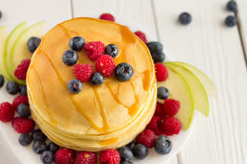 Stack of Sweet Pancakes with Fresh Blueberry, Raspberry, Apple and Maple Syrup on White Light Background, Top View